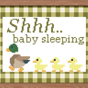 May include: Cross-stitch artwork in a wooden frame. The image features a duck leading three yellow ducklings, with the text "Shhh.. baby sleeping" above. The background has a green and white checkered pattern.