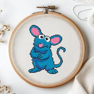 May include: A cross-stitch embroidery hoop showing a cartoon mouse. The mouse is blue with pink ears and a pink tongue. The embroidery is set in a wooden hoop, with a white background.
