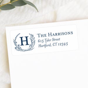 May include: A white rectangular label with navy blue text and a floral wreath design. The label includes the name "The Harrisons" and an address: 615 Tyler Street, Hartford, CT 12345. The letter "H" is inside the wreath.