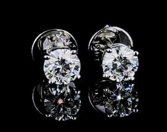 May include: A pair of silver stud earrings with a clear round gemstone in each. The earrings are set against a black background.