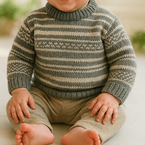 Puede incluir: Un bebé con un suéter de punto a rayas en tonos grises y beige. El suéter tiene cuello redondo y mangas largas. El bebé está sentado en el suelo con las piernas cruzadas.