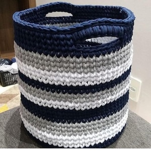 Peut inclure: Un panier de rangement en crochet rayé bleu et gris avec deux poignées.