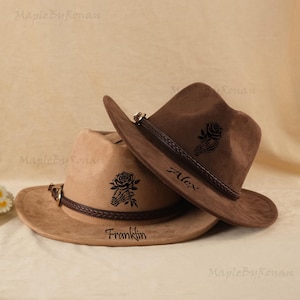 May include: Two brown cowboy hats with a rose and skeleton hand design. One hat is tan, the other is dark brown. The tan hat has the name "Franklin" and the dark brown hat has the name "Alex".