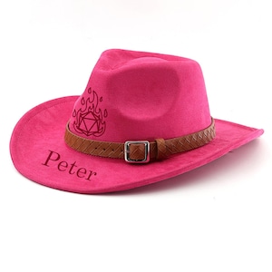 May include: A hot pink cowboy hat with a brown leather band and buckle. The hat has the name "Peter" printed on the brim and a flame and geometric design on the side.