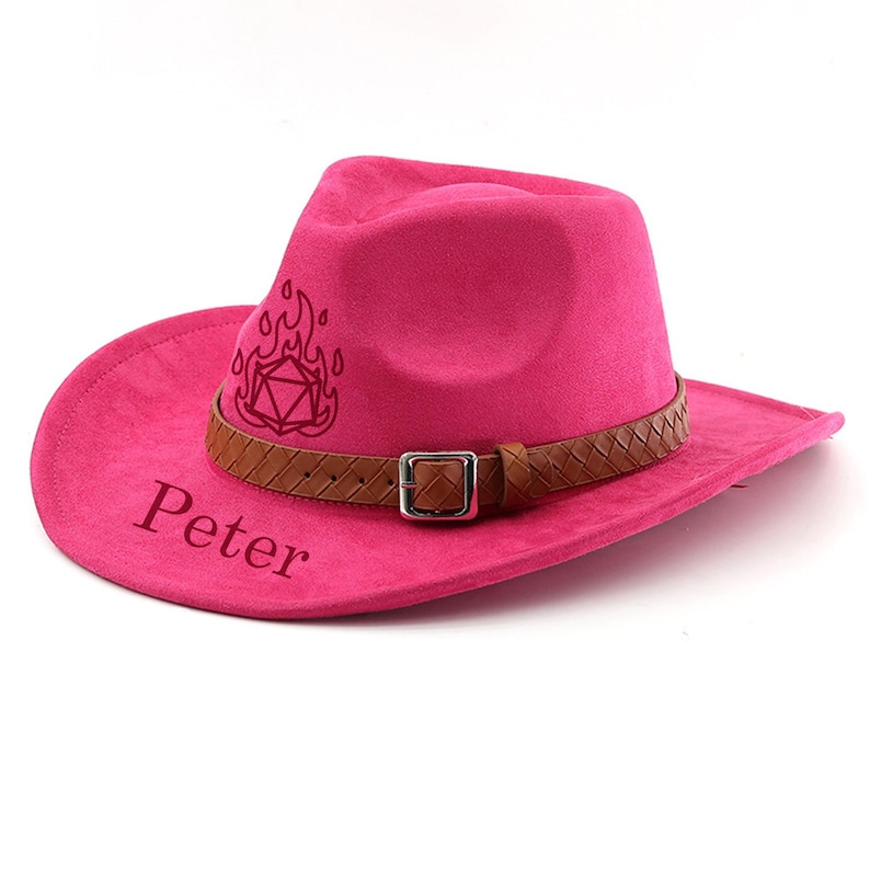 May include: A hot pink cowboy hat with a brown leather band and buckle. The hat has the name "Peter" printed on the brim and a flame and geometric design on the side.