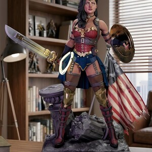 Könnte beinhalten: Detaillierte Statue von Wonder Woman, bekleidet mit einem rot-blauen Kostüm mit goldenen Akzenten, die ein Schwert und einen Schild hält. Die Figur steht auf einem Sockel mit einer zerfetzten amerikanischen Flagge im Hintergrund. Die Statue steht auf einem Holztisch.
