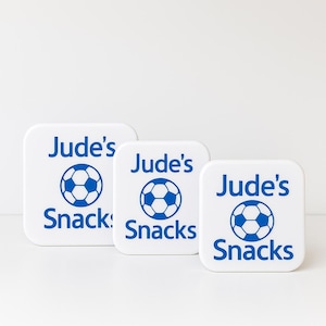 May include: Three white square snack containers with rounded corners. Each container has the text "Jude's Snacks" in blue, with a blue football graphic. The containers are in different sizes.