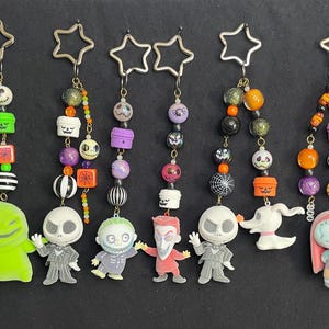 May include: A collection of Halloween-themed keychains featuring characters from The Nightmare Before Christmas. Each keychain has a star-shaped top and a beaded chain with character charms, including Jack Skellington, Sally, and Zero.