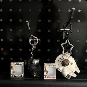 Può includere: Portachiavi con un personaggio di Batman nero e un Millennium Falcon, insieme a due personaggi Funko Pop!. Il portachiavi di Batman è nero e argento. Il portachiavi Millennium Falcon è bianco e marrone. I personaggi Funko Pop! sono in scatole trasparenti.