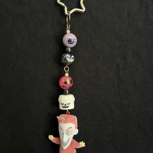 May include: A Nightmare Before Christmas themed keychain. The keychain features a silver star-shaped charm, colorful beads, and a Jack Skellington figure. The beads include a spider, a skull, and a pumpkin. The Jack Skellington figure is wearing a red suit.