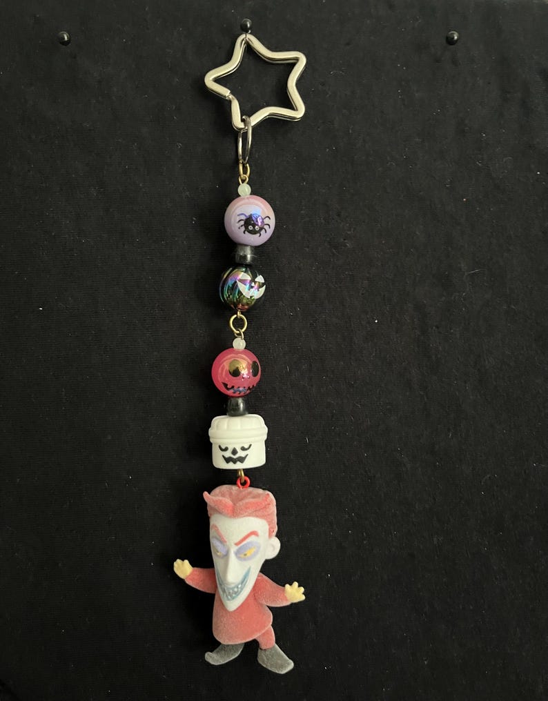 May include: A Nightmare Before Christmas themed keychain. The keychain features a silver star-shaped charm, colorful beads, and a Jack Skellington figure. The beads include a spider, a skull, and a pumpkin. The Jack Skellington figure is wearing a red suit.