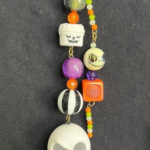 May include: A Halloween-themed keychain featuring a star-shaped top and a series of decorative beads. The beads include a green glitter ball, a white pumpkin, a purple glitter ball, a black and white ball, and a Jack Skellington figure.