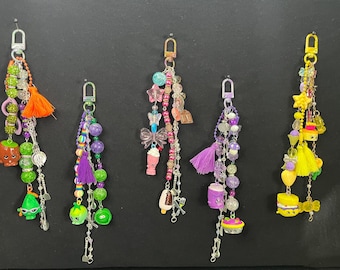 Könnte beinhalten: Fünf Schlüsselanhänger mit Charms, darunter Charaktere zum Thema Essen, Perlen und Quasten. Die Schlüsselanhänger haben eine Mischung aus Farben wie Grün, Lila, Orange und Gelb mit silberfarbenen Metallverschlüssen.