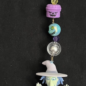 May include: A Nightmare Before Christmas themed charm. The charm features a star-shaped clasp, purple and clear beads, and a figurine of a character from the movie. The figurine is wearing a purple outfit and a witch hat.