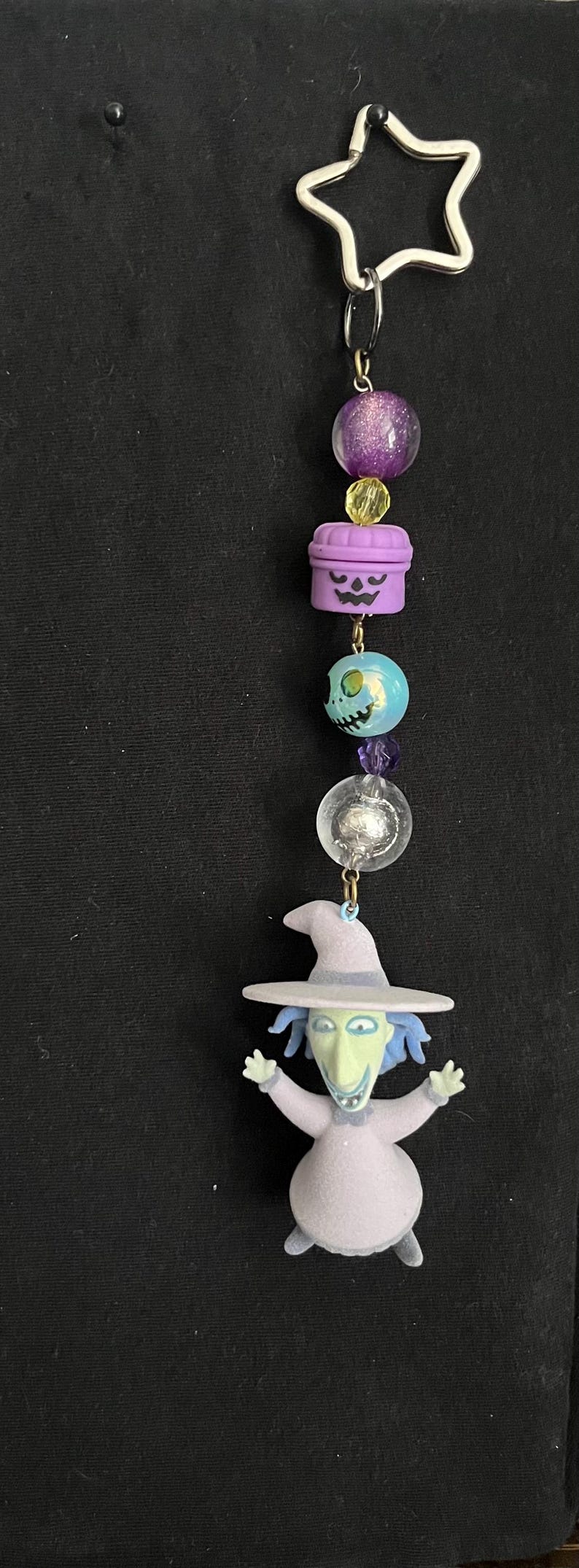 May include: A Nightmare Before Christmas themed charm. The charm features a star-shaped clasp, purple and clear beads, and a figurine of a character from the movie. The figurine is wearing a purple outfit and a witch hat.