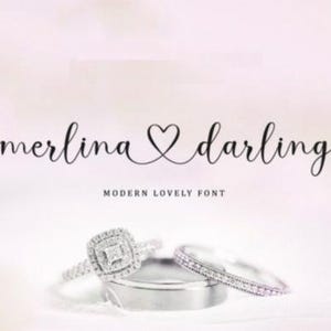Puede incluir: Un diseño de fuente cursiva con las palabras "merlina darling" y un símbolo de corazón entre las palabras. El texto está en negro sobre un fondo blanco. El texto está sobre dos anillos plateados.