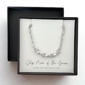 Puede incluir: Un brazalete plateado con cristales transparentes y perlas de imitación, presentado en una caja de regalo negra. La caja contiene una tarjeta blanca con el texto "Step Mum of the Groom, Thank you for Everything."