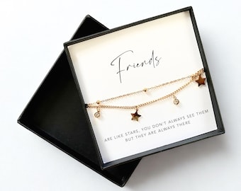 May include: A gold-colored, double-layered bracelet with star and crystal charms, presented in a black gift box. The card inside reads "Friends" with the quote "ARE LIKE STARS, YOU DON'T ALWAYS SEE THEM BUT THEY ARE ALWAYS THERE."