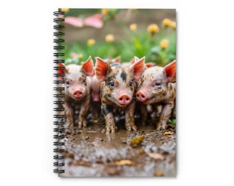 Könnte beinhalten: Spiralgebundenes Notizbuch mit einem Foto von drei Ferkeln im Schlamm. Die Ferkel haben rosa Schnauzen und Ohren mit schwarzen und braunen Flecken. Der Hintergrund ist verschwommen mit grünem Laub und gelben Blumen.