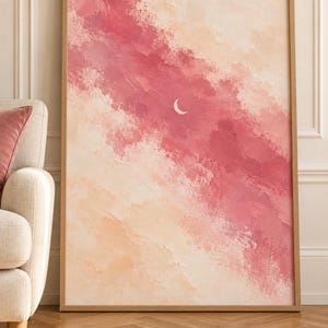 Könnte beinhalten: Ein rechteckiger Wandkunstdruck in einem hellen Holzrahmen mit einem abstrakten Gemälde eines Himmels mit strukturierten Pinselstrichen in Rosa-, Pfirsich- und Cremetönen. Ein kleiner, dünner weißer Halbmond befindet sich in der Mitte.