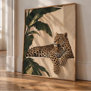 Può includere: Una stampa artistica quadrata incorniciata che raffigura un leopardo a riposo su una sporgenza in pietra beige. Il leopardo ha il manto maculato ed è posizionato tra grandi foglie di palma tropicale verde scuro su una parete beige.