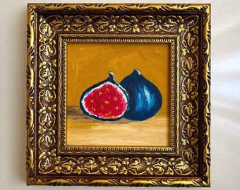 May include: An oil painting of two figs, one halved to reveal a bright red interior and one whole dark blue fig, set against a mustard yellow background. The artwork is encased in a square, ornate, dark brown and gold-toned decorative frame.