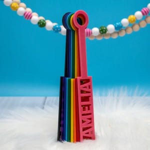 May include: A rainbow-colored, multi-layered, plastic name tag with the name "AMELIA" printed in pink letters.