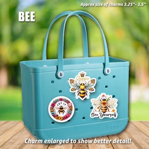 May include: A light blue tote bag with three bee-themed charms. The charms are approximately 3.25 inches to 3.5 inches in size. The charms feature bees, flowers, and the text "Queen", "Let It Bee", and "Bee Yourself".