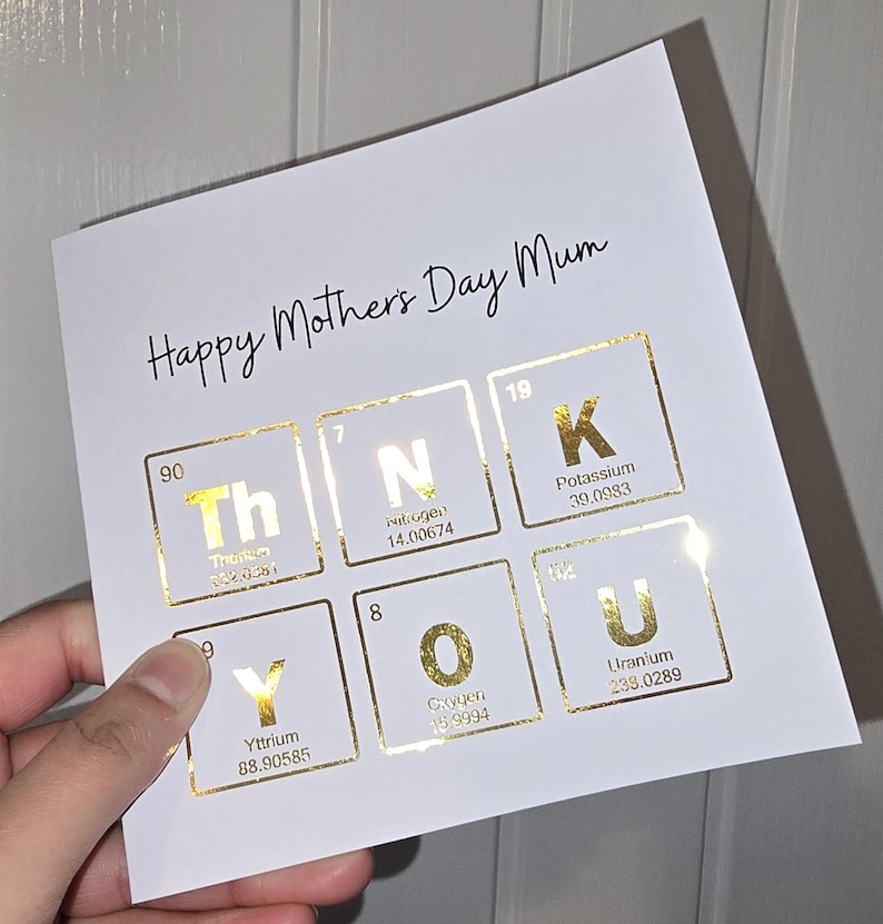 Peut inclure: Une carte de v&oelig;ux carr&eacute;e blanche avec le texte noir Happy Mothers Day Mum en haut. En dessous, six &eacute;l&eacute;ments du tableau p&eacute;riodique en feuille d'or &eacute;pellent THANK YOU, avec les symboles Th, N, K, Y, O, U, leurs num&eacute;ros et noms atomiques.