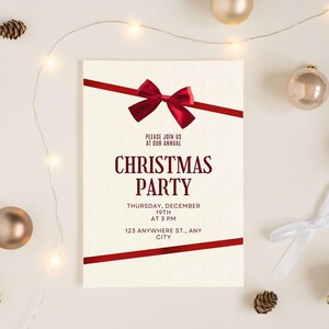 Pode incluir: Um convite creme para uma festa de Natal com fitas vermelhas e um laço. O convite diz "CHRISTMAS PARTY" com a data, hora e endereço. Elementos decorativos incluem enfeites de Natal e pinhas.