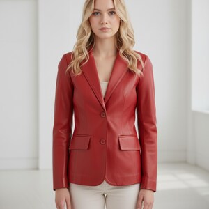May include: A red leather blazer with a notched lapel, two-button closure, and two front pockets. The blazer is a solid color and appears to be well-tailored. The model is wearing a cream-colored top and pants.