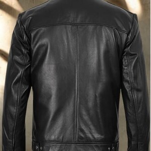 May include: A black leather jacket with a classic design. The jacket features a collared neckline, long sleeves, and a button-down front. The back of the jacket has a simple, clean design. The jacket is made of a smooth, shiny leather material.