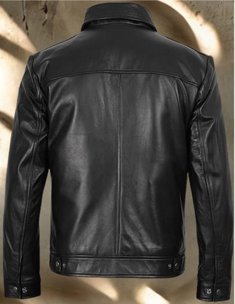 May include: A black leather jacket with a classic design. The jacket features a collared neckline, long sleeves, and a button-down front. The back of the jacket has a simple, clean design. The jacket is made of a smooth, shiny leather material.