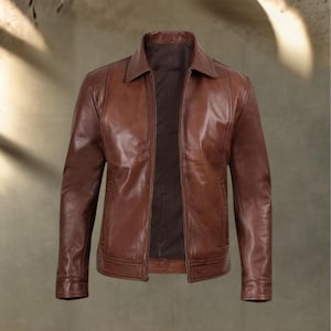 May include: A brown leather jacket with a collared neckline and a zipper closure. The jacket has a classic design with a tailored fit, featuring pockets and a smooth, glossy finish. The jacket is a medium brown color.