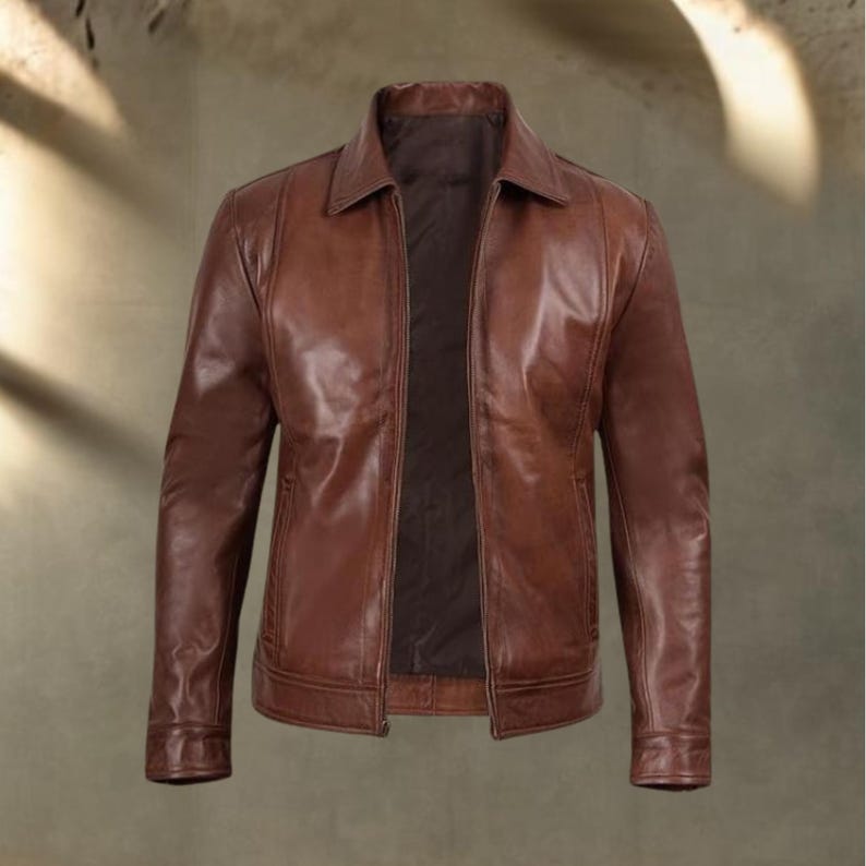 May include: A brown leather jacket with a collared neckline and a zipper closure. The jacket has a classic design with a tailored fit, featuring pockets and a smooth, glossy finish. The jacket is a medium brown color.