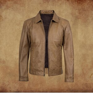 May include: A tan leather jacket with a collared neckline and a zipper closure. The jacket has two front pockets and a dark brown interior lining. The jacket is displayed on a brown background.