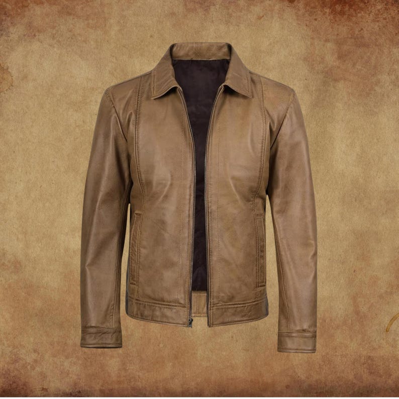 May include: A tan leather jacket with a collared neckline and a zipper closure. The jacket has two front pockets and a dark brown interior lining. The jacket is displayed on a brown background.