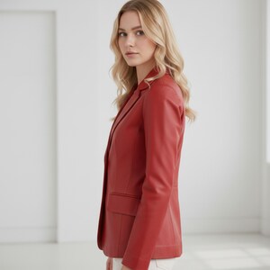 May include: A red blazer with a classic design. The blazer features a notched lapel, a two-button closure, and a single chest pocket. The sleeves are long, and the blazer is made of a smooth material. The model is wearing white pants.