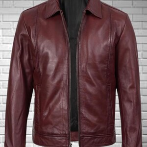 May include: A burgundy leather jacket with a collared neckline and a full-length zipper. The jacket has two front pockets and a black interior lining. The leather has a smooth texture and a slight sheen.