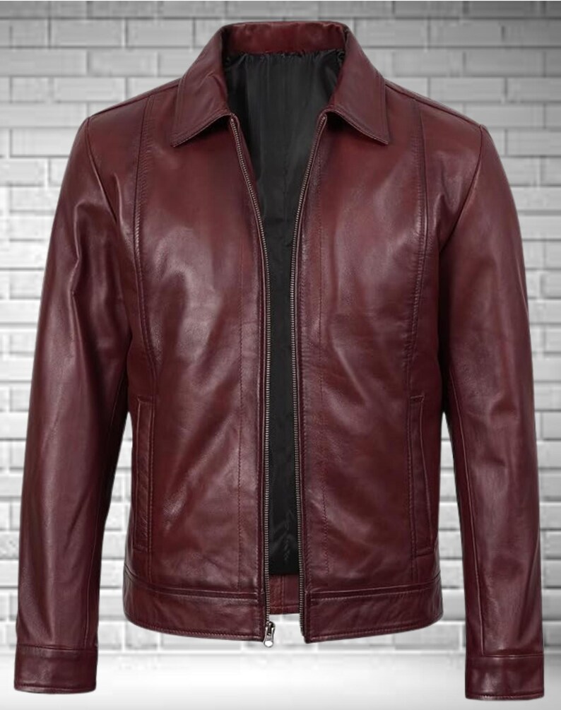 May include: A burgundy leather jacket with a collared neckline and a full-length zipper. The jacket has two front pockets and a black interior lining. The leather has a smooth texture and a slight sheen.