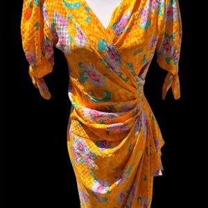 May include: A yellow wrap dress with a floral print. The dress has a V-neckline and short sleeves with puffed shoulders. The dress is cinched at the waist and has a flowing skirt.