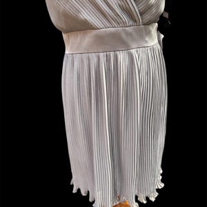 May include: A light gray pleated dress with a V-neckline and a sash at the waist.