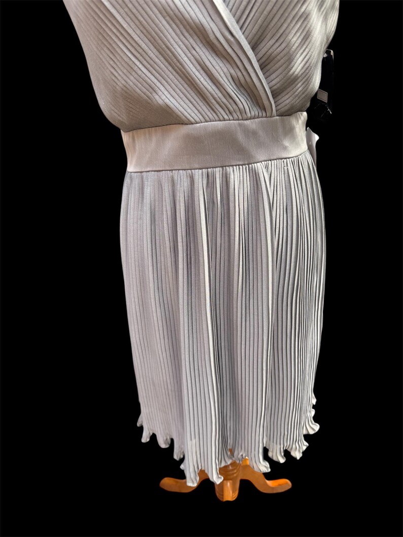 May include: A light gray pleated dress with a V-neckline and a sash at the waist.