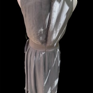 May include: A gray pleated sleeveless dress with a fitted bodice and a flowing skirt. The dress has a belt at the waist and a scalloped hem.