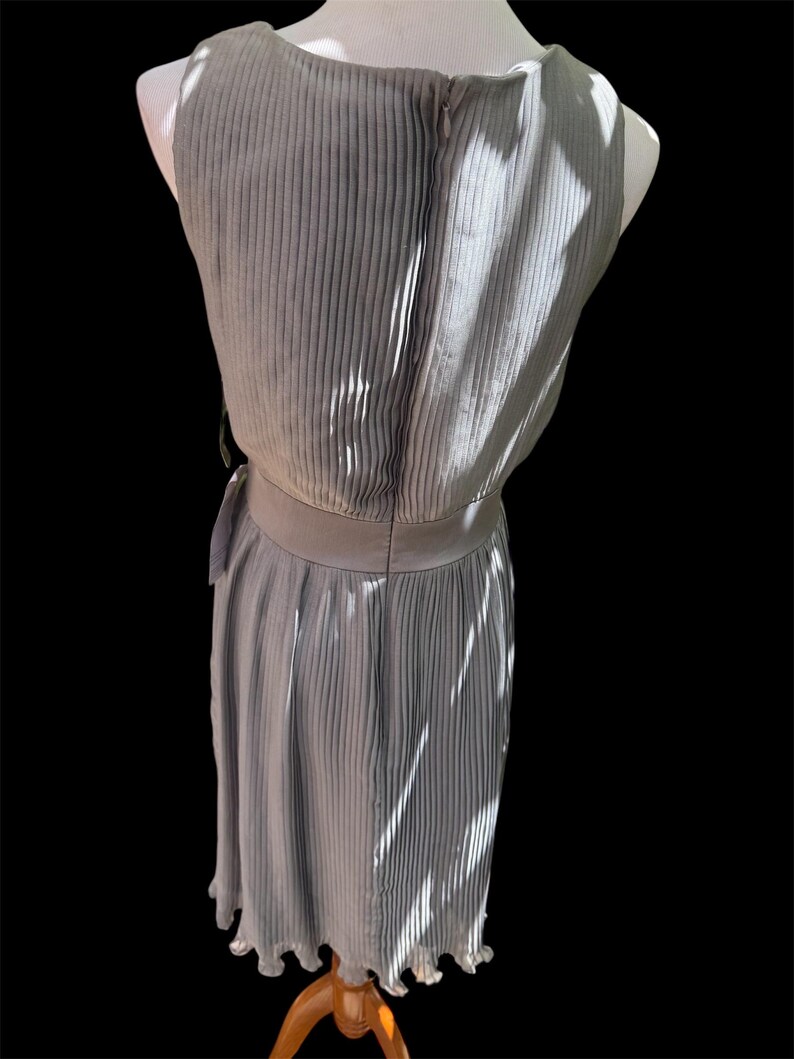 May include: A gray pleated sleeveless dress with a fitted bodice and a flowing skirt. The dress has a belt at the waist and a scalloped hem.