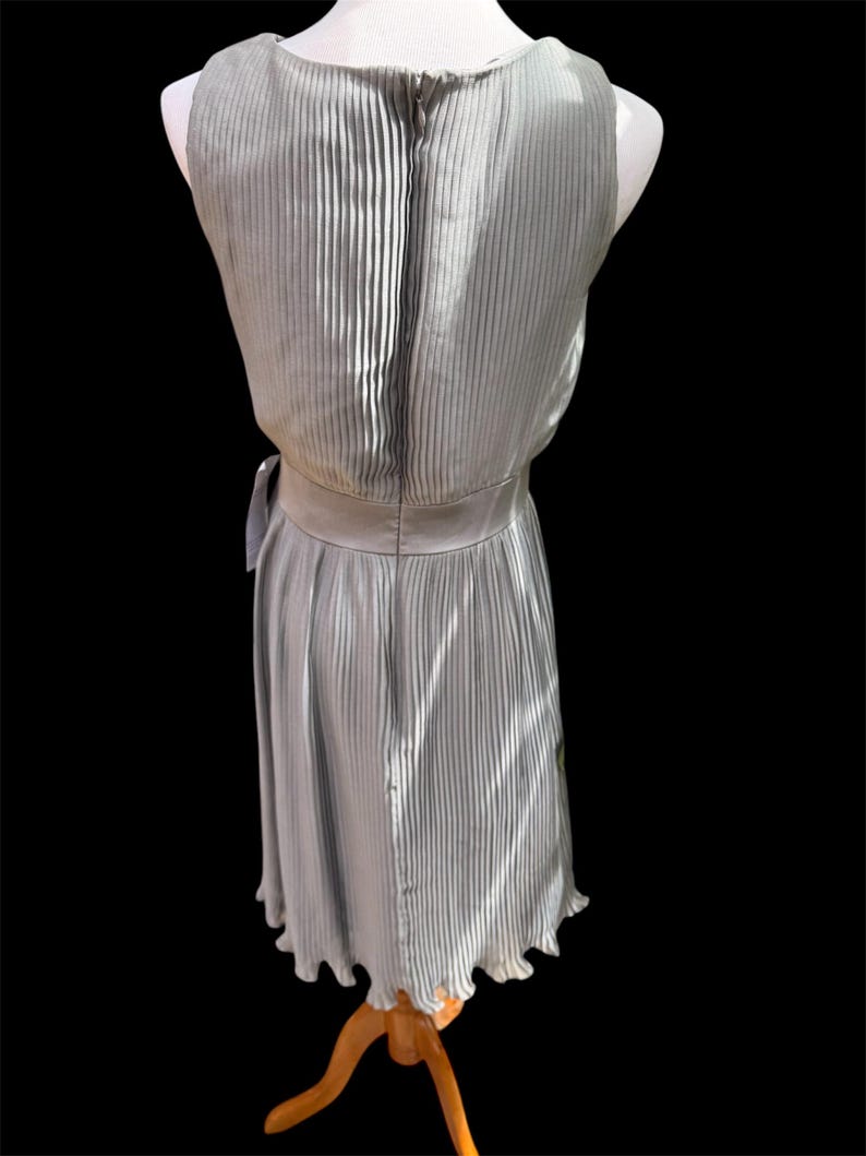 May include: A silver pleated sleeveless dress with a back zipper and a tie at the waist.