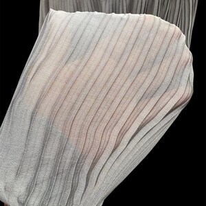 May include: A close-up of a gray pleated skirt made of a sheer fabric. The pleats are evenly spaced and create a delicate, flowing look.