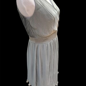 May include: A sleeveless, light gray, pleated dress with a V-neckline and a scalloped hem.