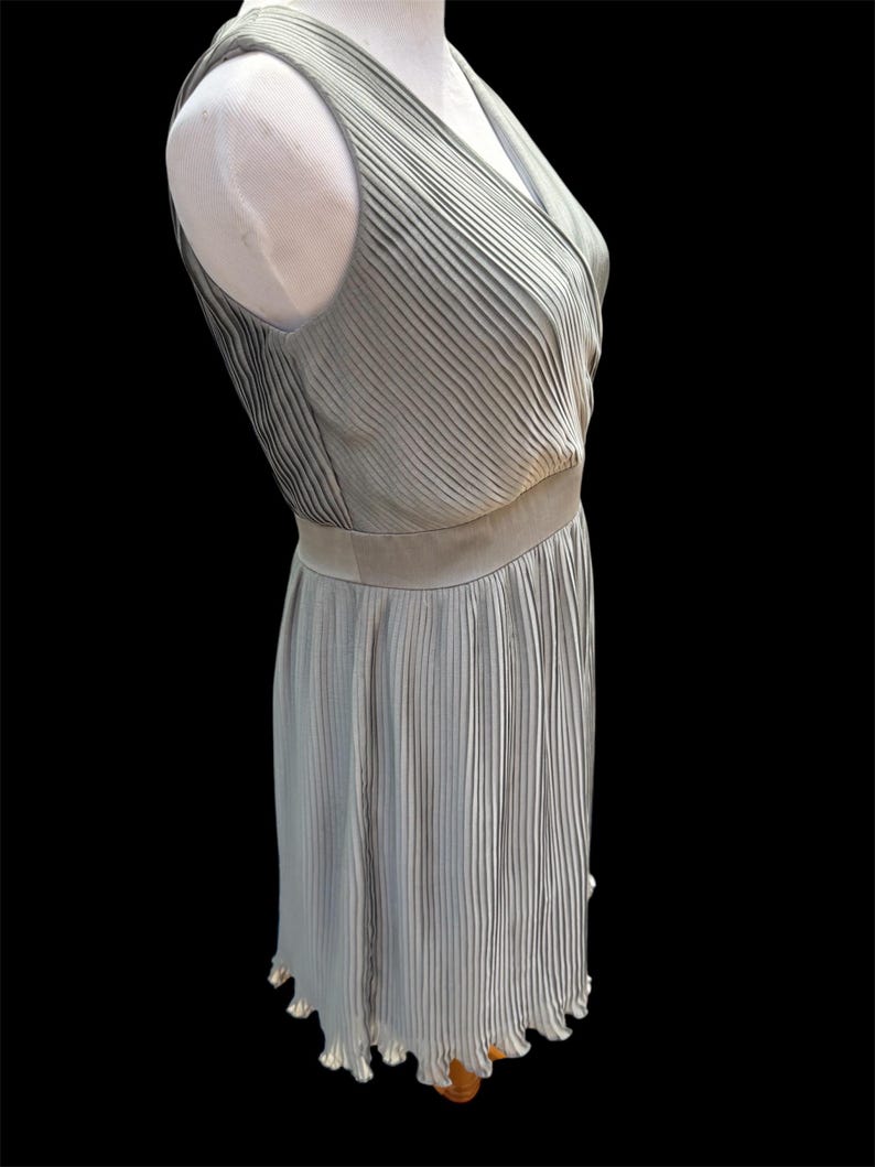 May include: A sleeveless, light gray, pleated dress with a V-neckline and a scalloped hem.