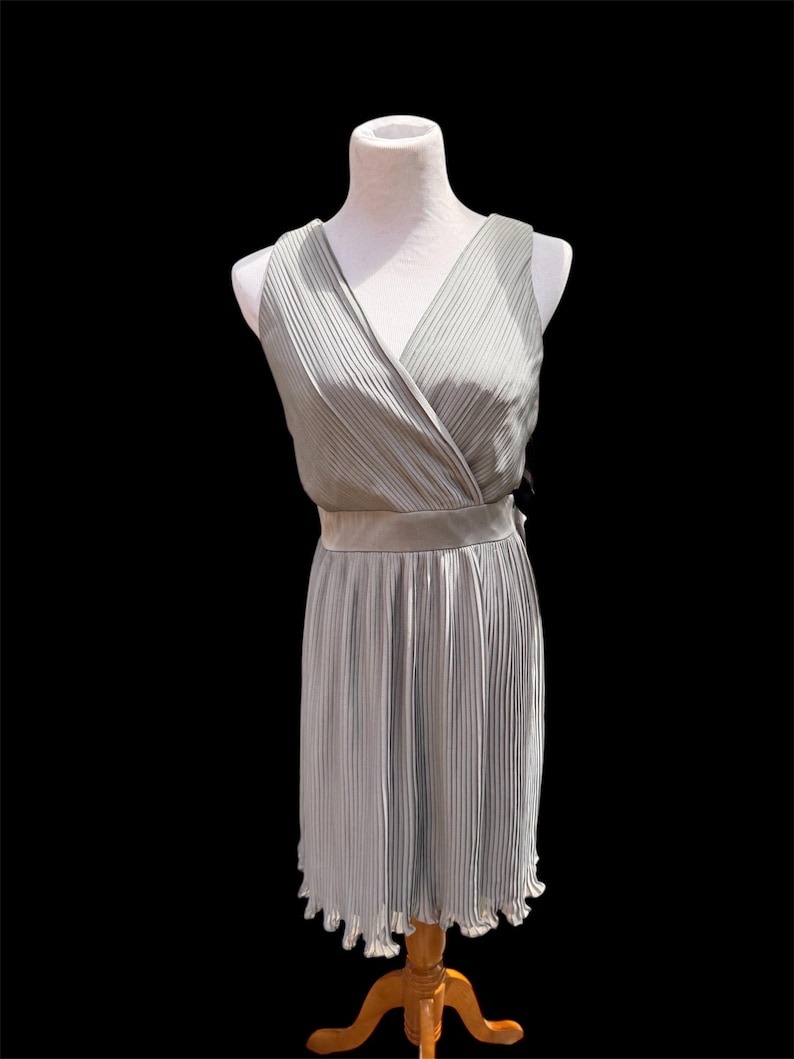 May include: A sleeveless, light gray, pleated dress with a V-neckline and a ruffled hem.